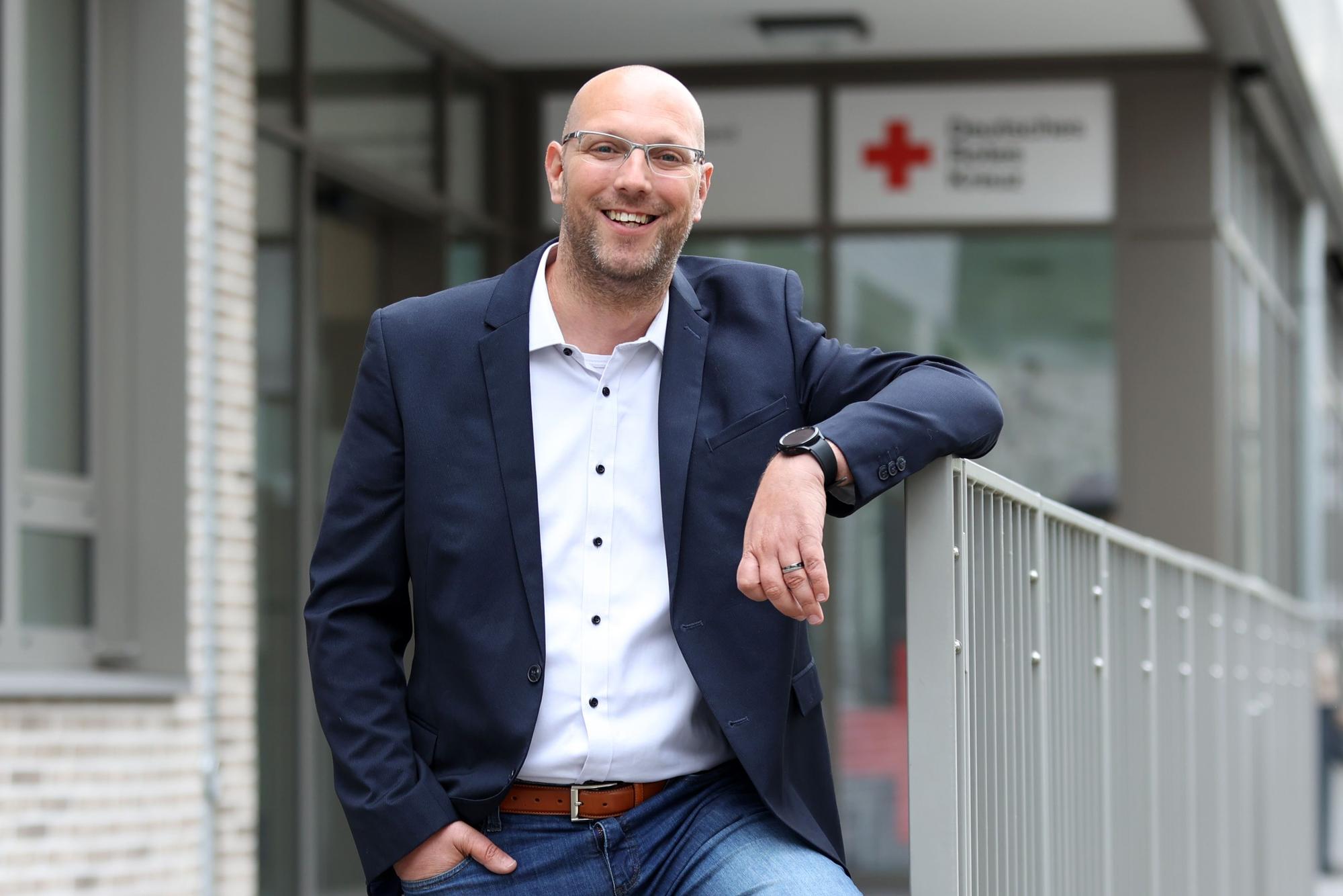 Marcel Pertsemlis, Bereichsleitung Hausnotruf, Fachbereich Senioren und Behinderte beim DRK, steht vor dem Gebäude des DRK in Köln Ehrenfeld.