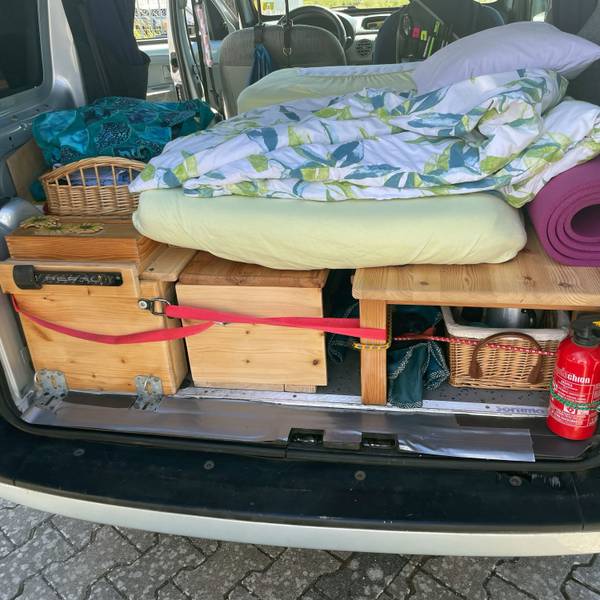 Das Bild zeigt den hinteren Bereich eines Renault Kangoo. Mit Holzaufbauten ist eine Schlaffläche samt Stauraum entstanden. Darauf liegt eine Matratze.