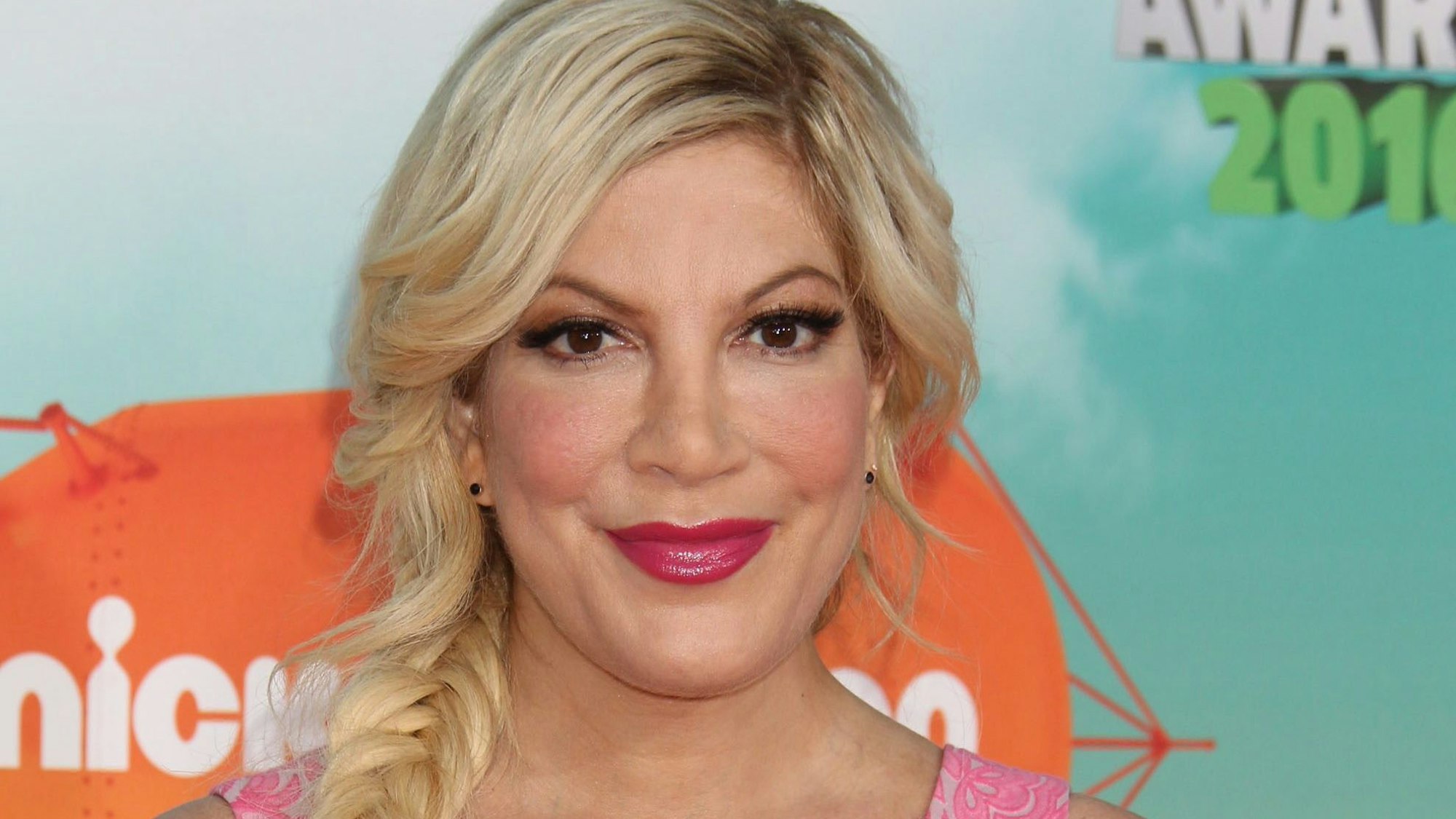 Tori Spelling posiert vor einer Fotowand.