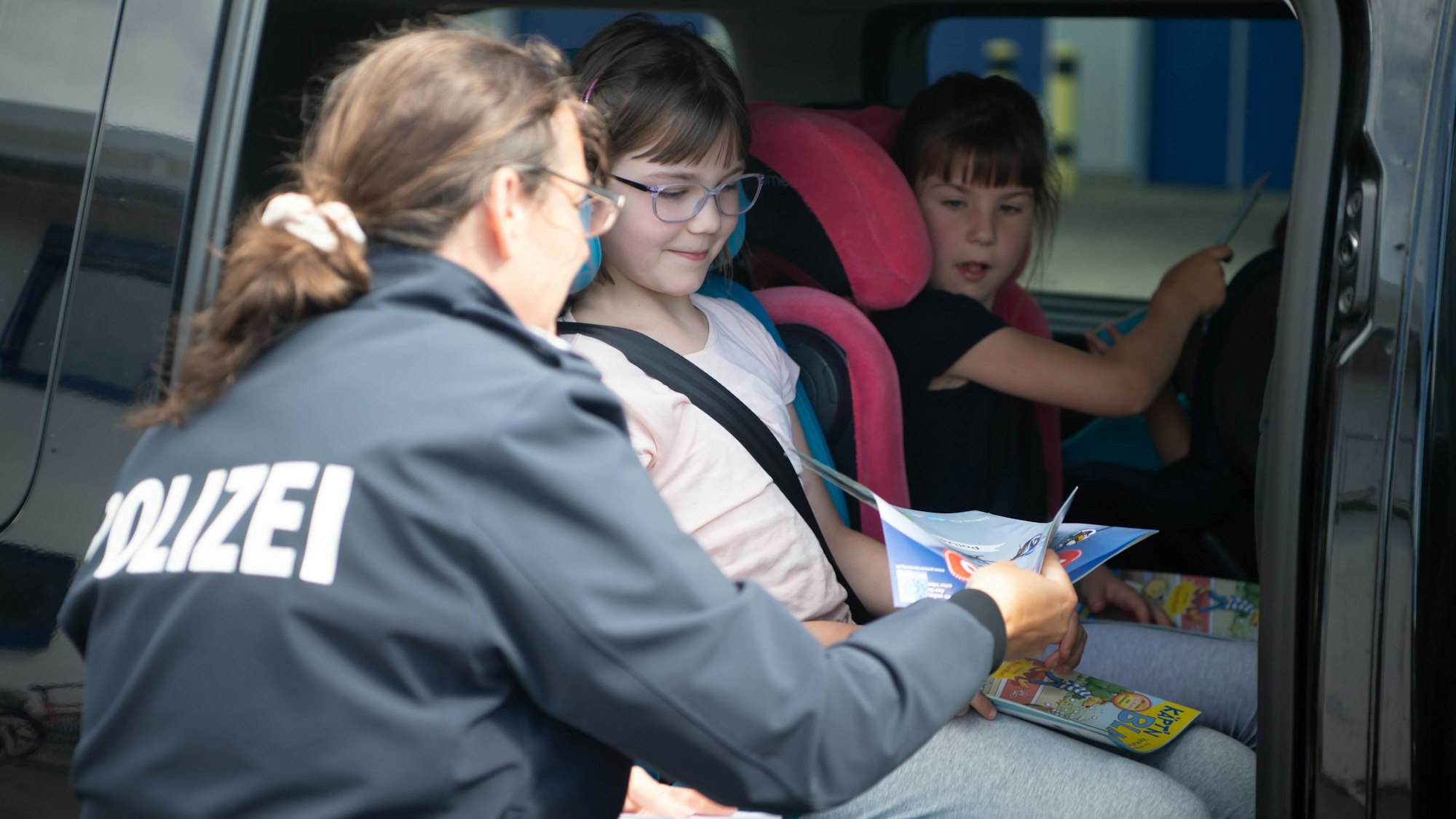 Das Bild zeigt eine Polizeibeamtin, die zwei Mädchen etwas Lesematerial für die Fahrt in Urlaub überreicht.