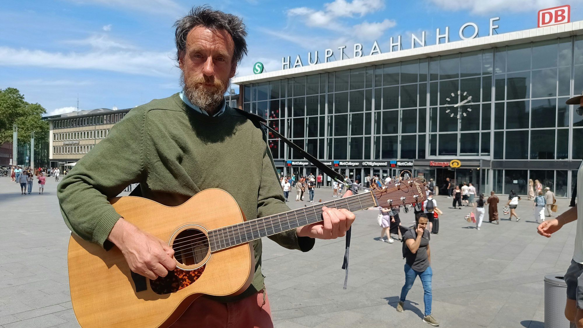 Ein Mann mit Gitarre steht vor dem Kölner Hauptbahnhof.