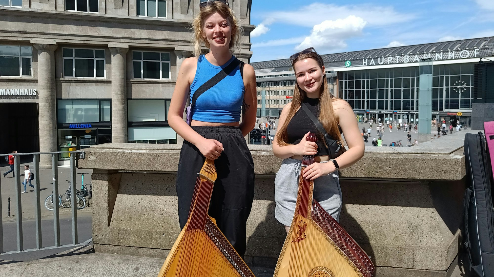 Zwei Frauen mit gitarrenähnlichen Musikinstrumenten stehen im Schatten des Kölner Doms.