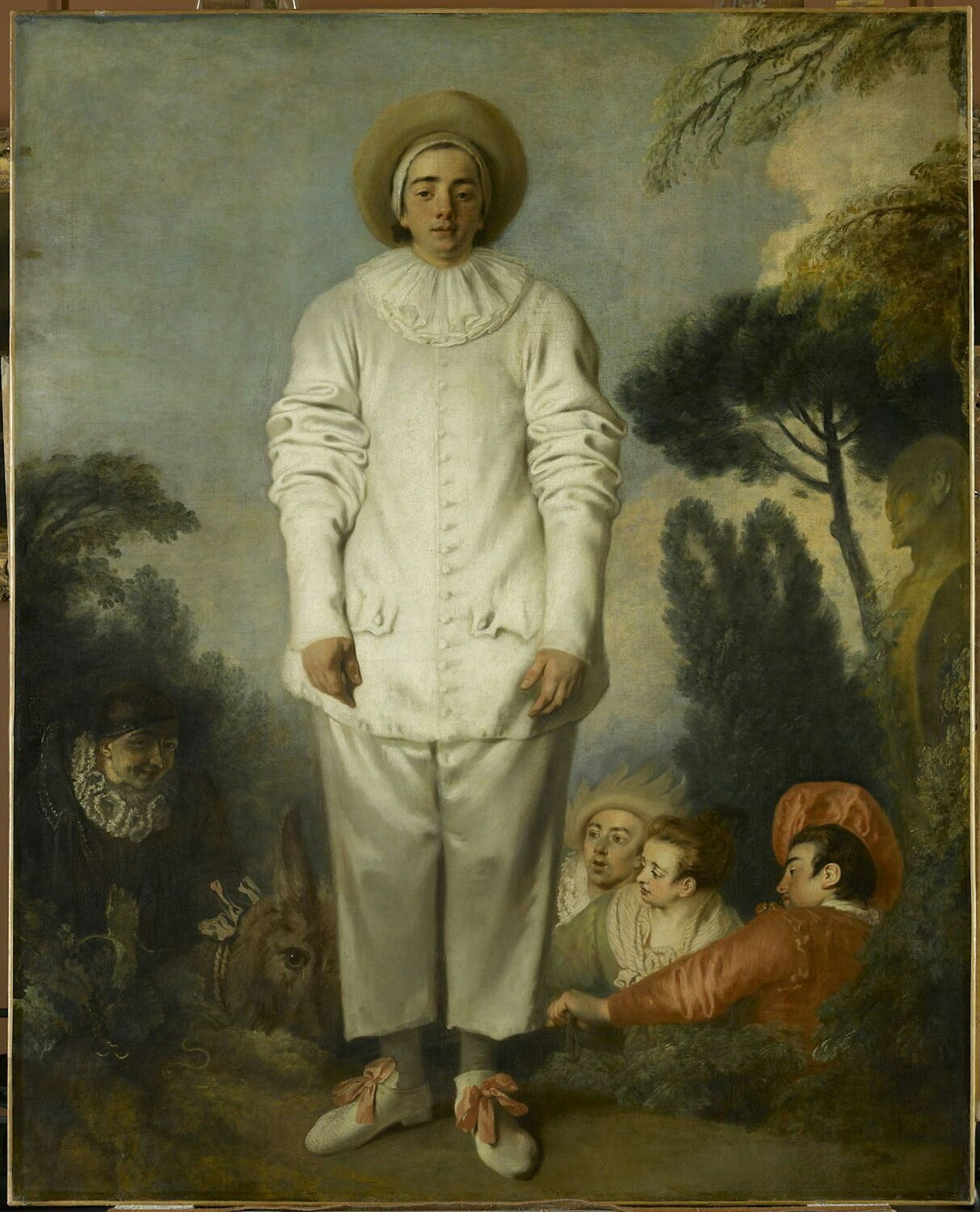 Ein Clown steht auf einer Bühne, während im Hintergrund Schauspieler Faxen machen.