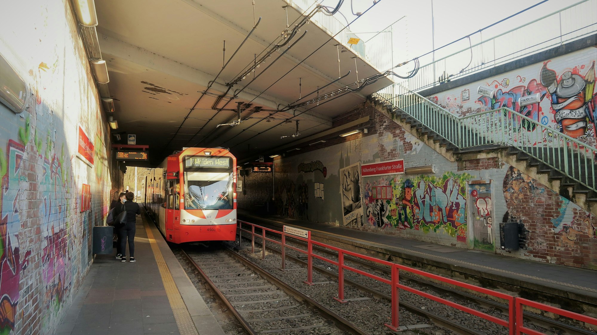 Eine Bahn der Linie 1 an einer Haltestelle, deren Wände Graffities zieren.
