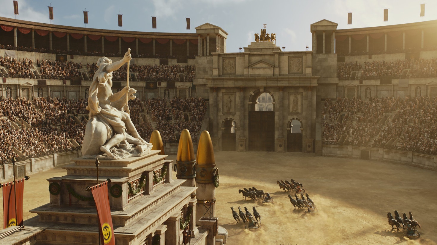 Auf dem Bild ist eine große Arena zu sehen. Es findet ein Wagenrennen statt. Die Wagen fahren um ein Monument inmitten der Arena herum, darauf thront eine Statue.