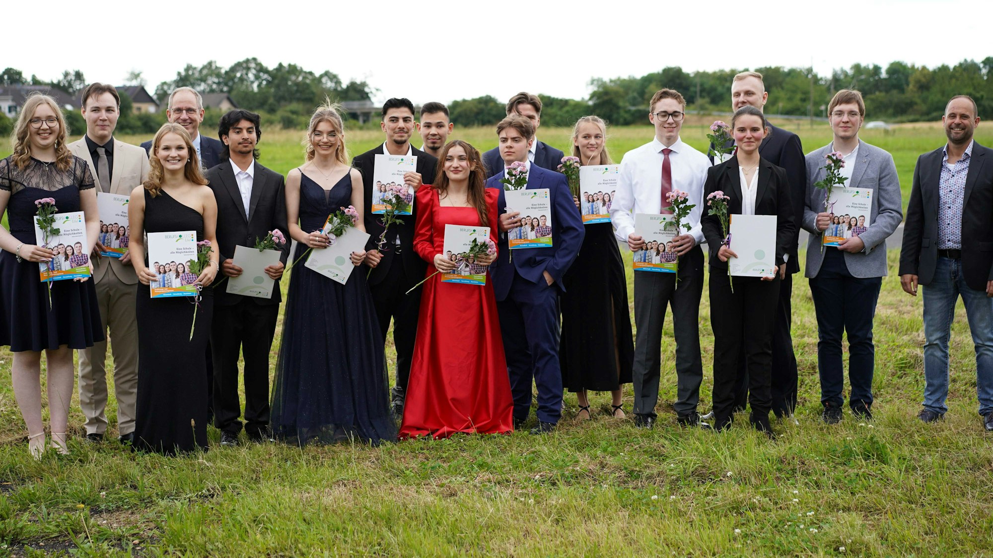 Der Abiturjahrgang des Berufskolleg Eifel steht in Abendgarderobe auf einer Wiese.