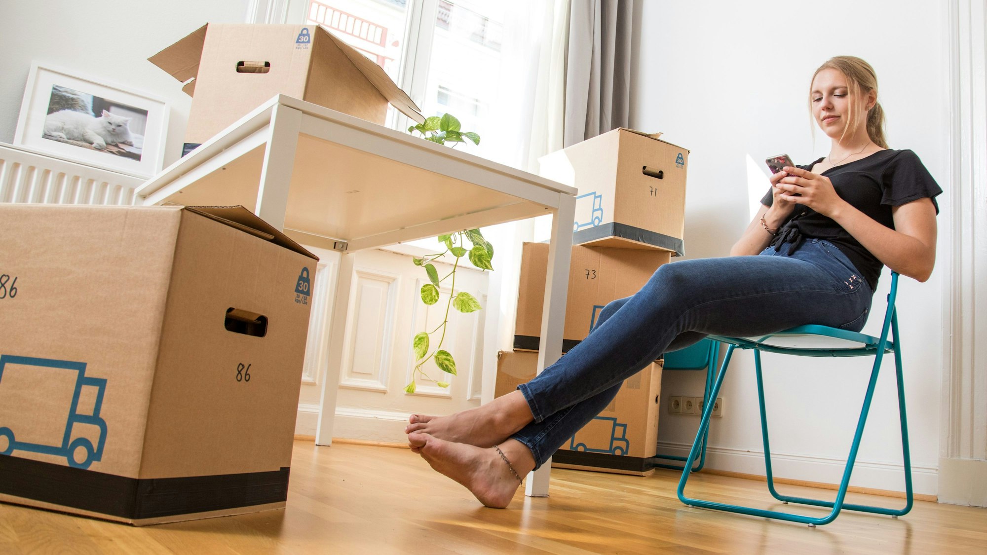 Eine Frau sitzt zwischen Umzugskartons in einer Wohnung auf einem Klappstuhl.