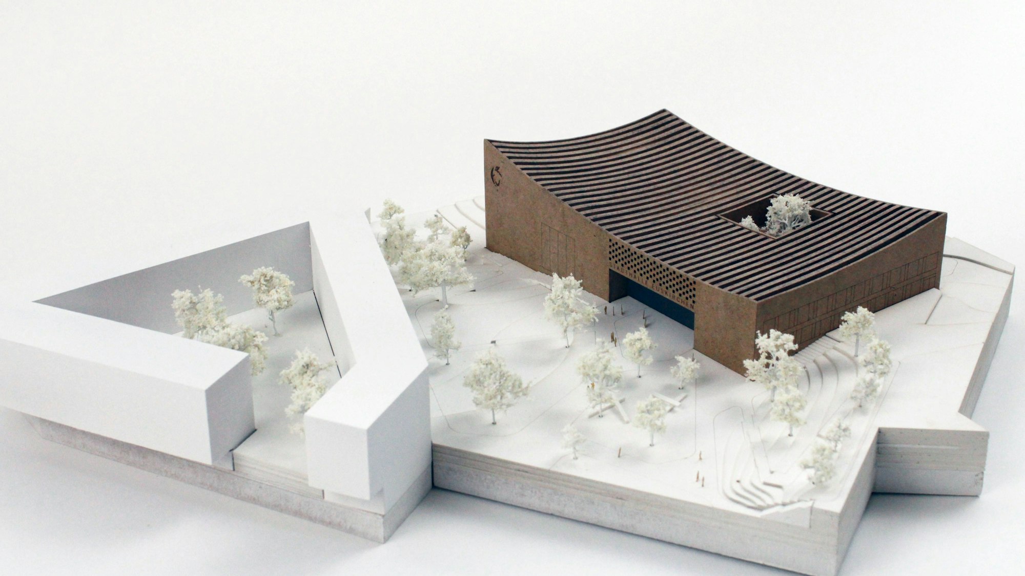 Das Gebäude in einem dunklen Holzton hat ein leicht geschwungenes Flachdach, in einem Innenhof stehen zwei Bäume.