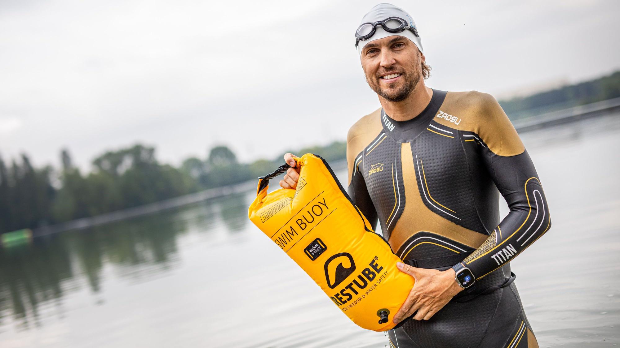 Der Schwimmtrainer und Athlet Johann Ackermann zeigt eine Schwimmboje von Restube im Wasser am Ufer des Fühlinger See. Ackermann gibt unter dem Namen „Der Schwimmcoach“ regelmäßig Workshops für Triathleten, bei denen es um das Freiwasserschwimmen geht.