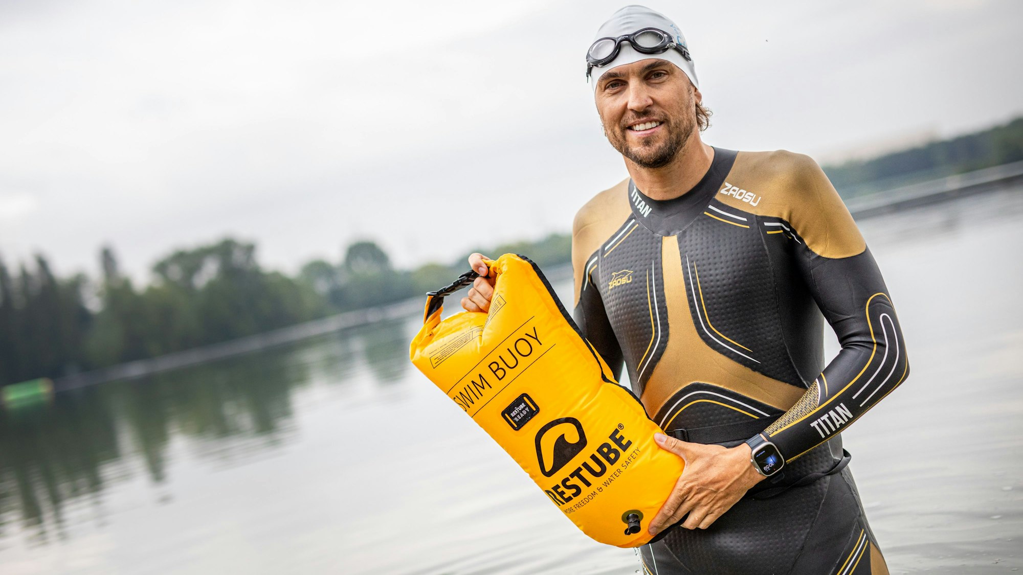 Der Schwimmtrainer und Athlet Johann Ackermann zeigt eine Schwimmboje von Restube im Wasser am Ufer des Fühlinger See. Ackermann gibt unter dem Namen „Der Schwimmcoach“ regelmäßig Workshops für Triathleten, bei denen es um das Freiwasserschwimmen geht.