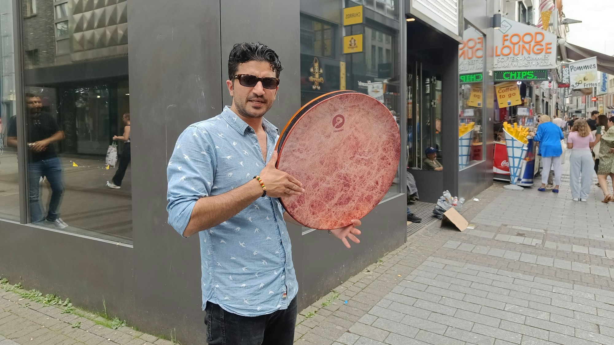 Ein Mann mit Hemd, Sonnenbrille und Trommel steht auf der Hohe Straße.