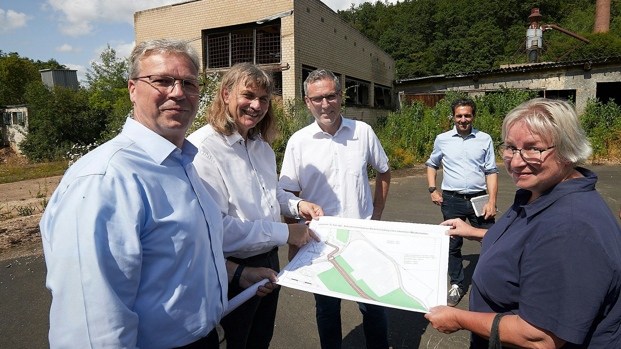 Die Beteiligten stehen auf dem Gelände und breiten einen Lageplan aus.