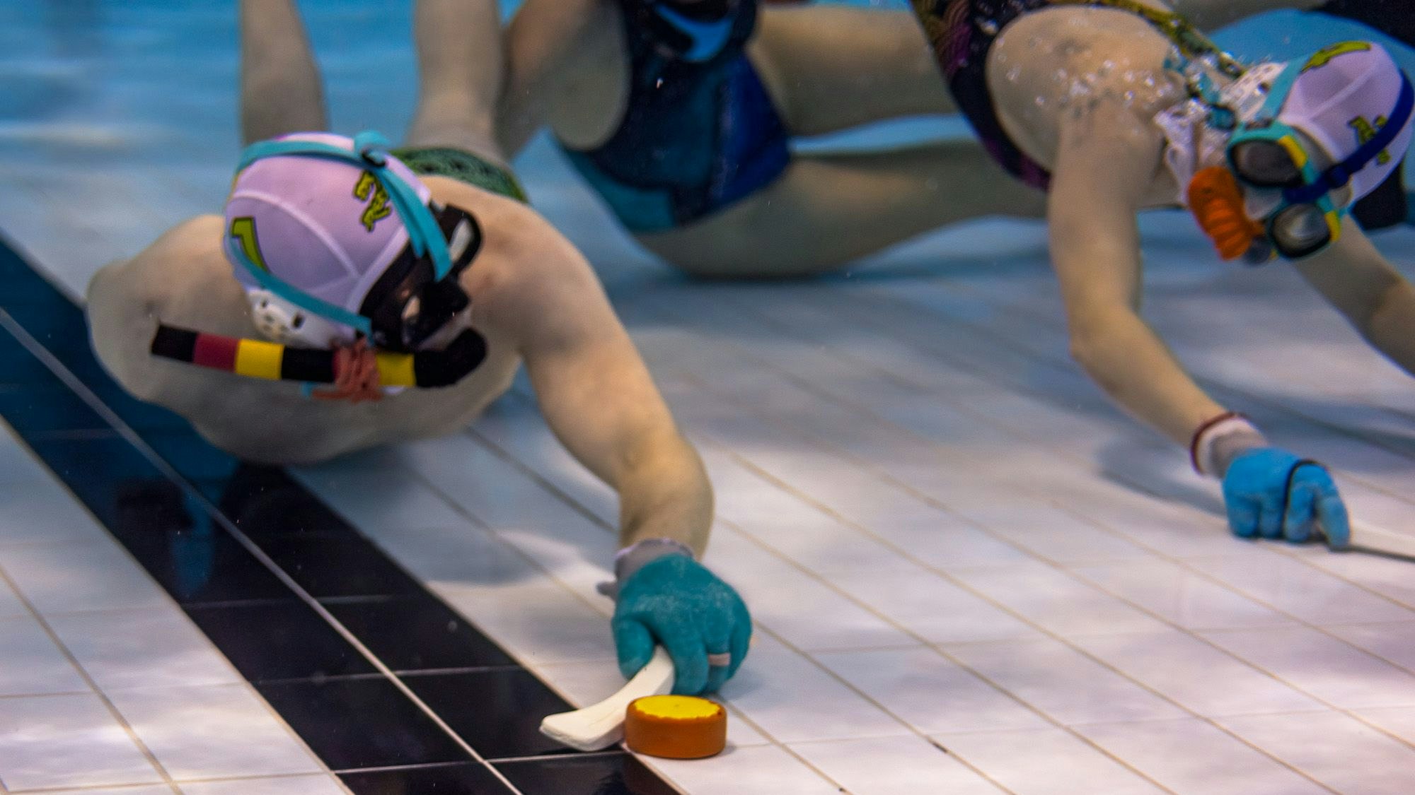 Spieler mit Badekappen und Schlägern spielen Unterwasserhockey.