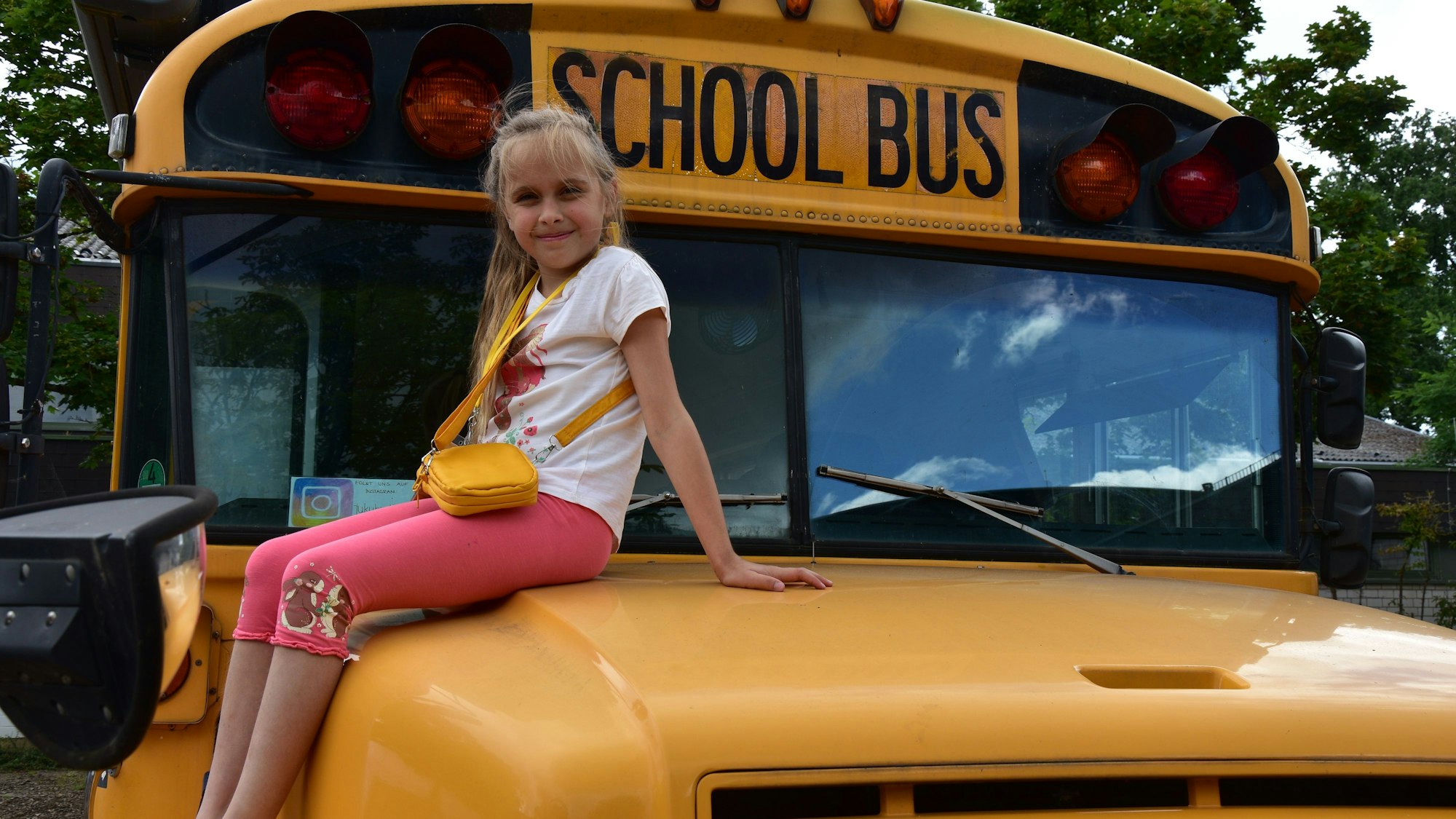 Ein Mädchen sitzt auf der Motorhaube eines amerikanischen Schulbusses.