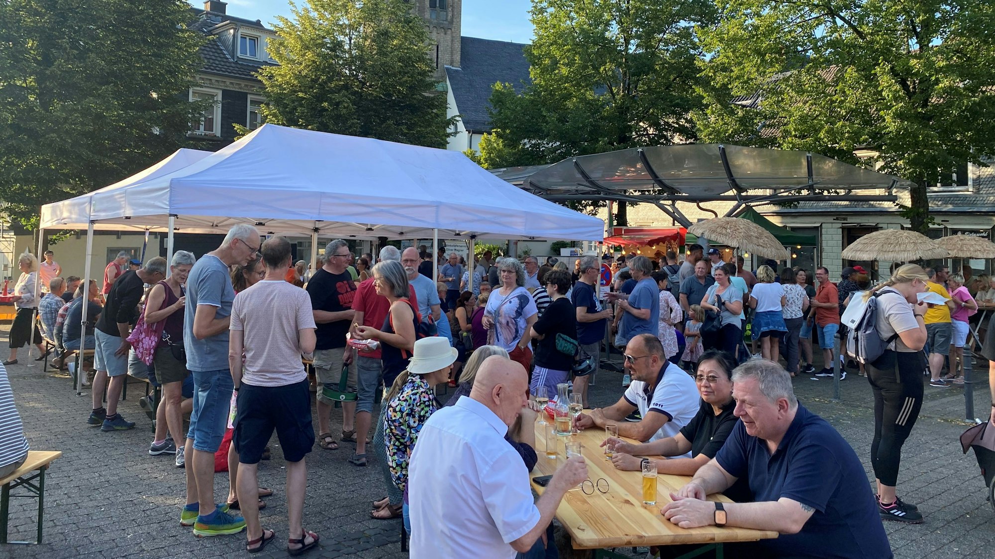 Menschen sitzen an Tischen und stehen unter Pavillons auf dem Burscheider Marktplatz.
