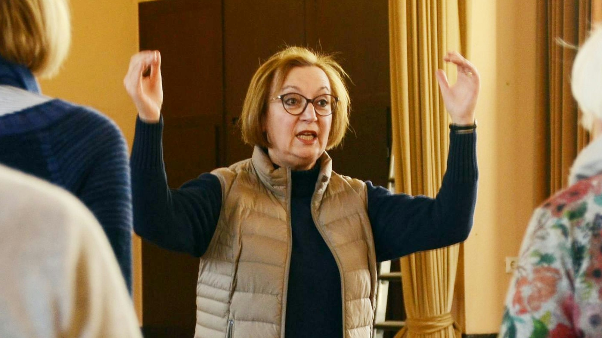 Eine Frau dirigiert einen Chor, dabei singt sie auch selbst.