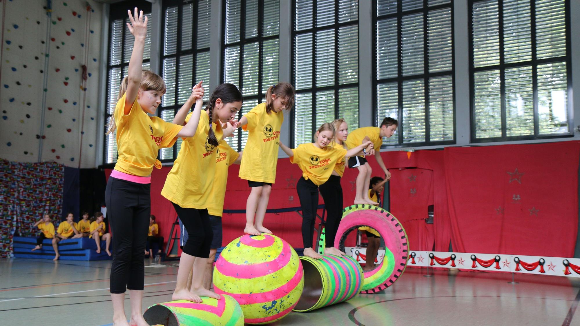 Sechs Kinder balancieren auf bunten Bällen und Rollen.