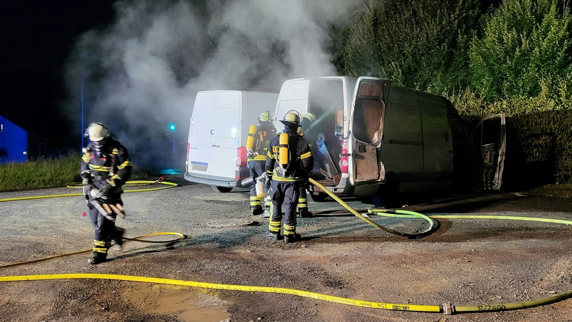 Feuerwehrleute löschen einen Transporter, dessen Laderaum geöffnet ist.