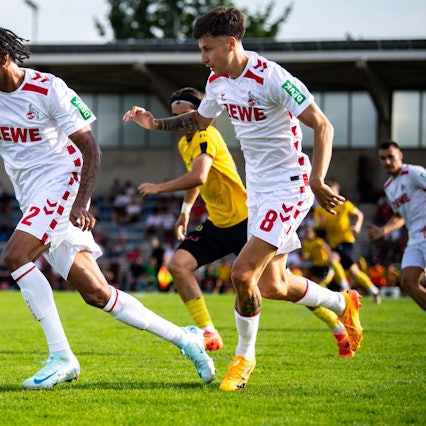 Das Bild zeigt den Fußballspieler des 1. FC Köln, Damion Downs (l.), wie er den Ball im Mittelfeld vorantreibt.