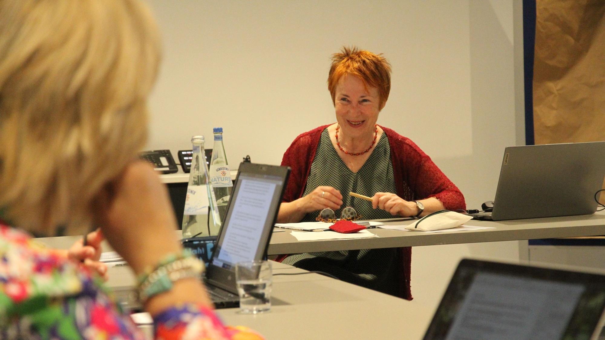 Eine Frau mit kurzen roten Haaren an einem Tisch mit Notebook