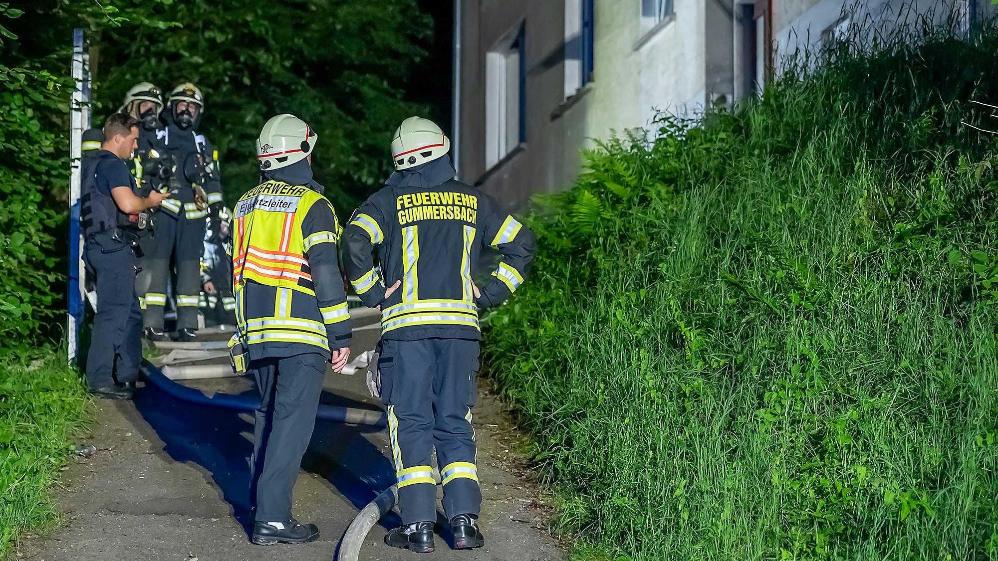 Mehrere Feuerwehrleute stehen vor einem Gebäude, in dem es gebrannt hat.