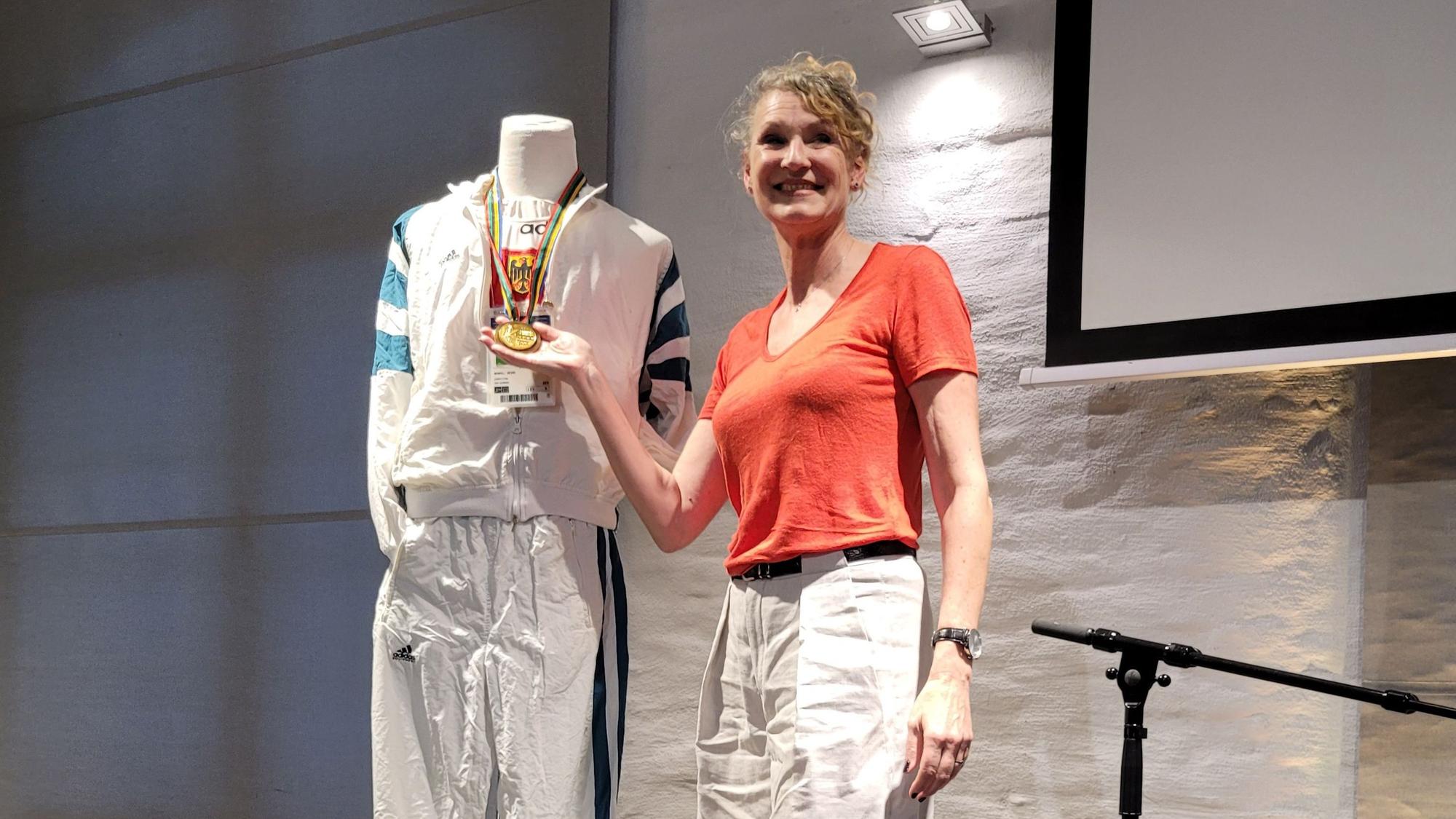 Eine Frau hält eine Goldmedaille in der Hand.