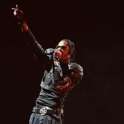 Travis Scott während seiner Circus Maximus' Tour in Kalifornien. Er ist ganz in Schwarz gekleidet und reckt die rechte Hand in die Höhe.