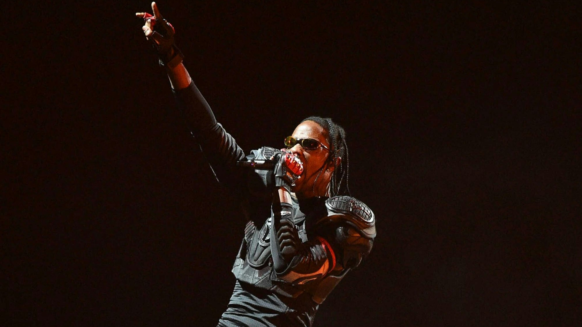 Travis Scott während seiner Circus Maximus' Tour in Kalifornien. Er ist ganz in Schwarz gekleidet und reckt die rechte Hand in die Höhe.