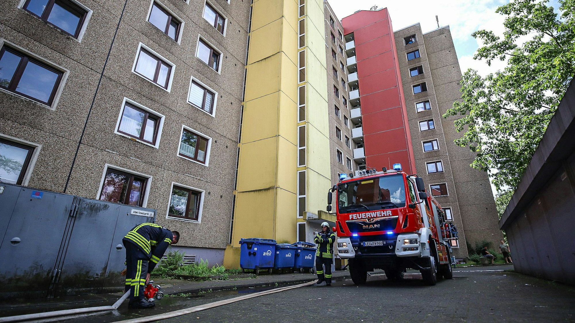 Feuerwehrleute rollen einen Schlauch an einem Hochhaus aus.
