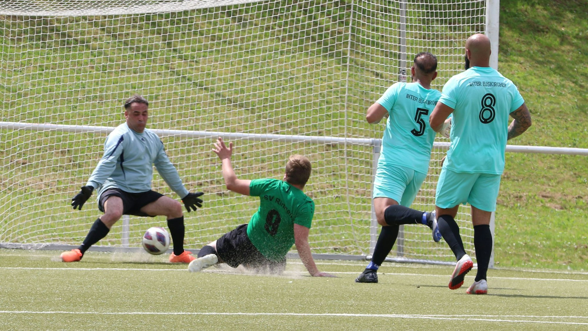 Ein Stürmer schiebt liegend den Ball zum Tor ein. Dabei bleibt der Torwart offenbar im Rasen hängen und verletzt sich.