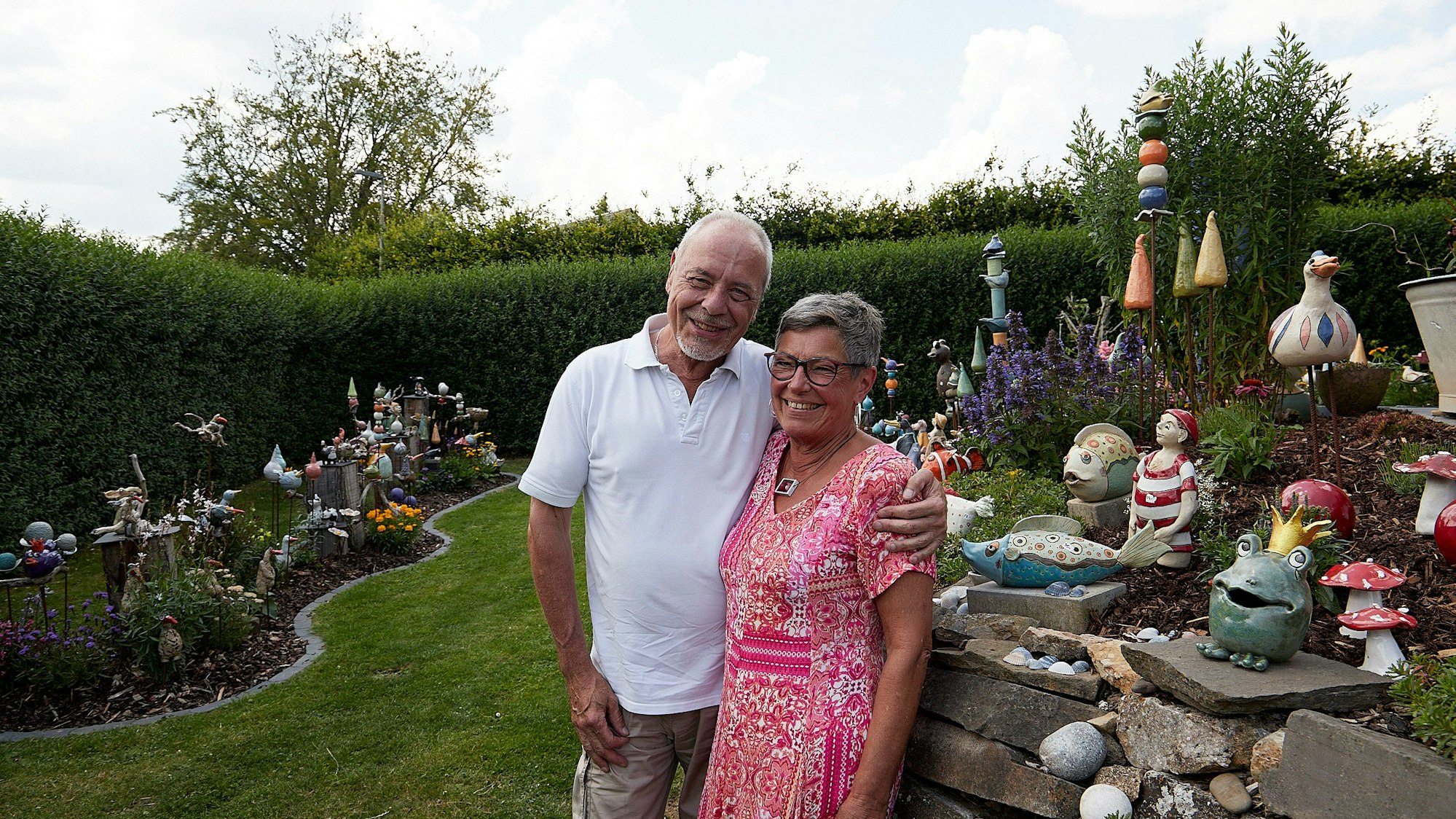 Klara und Rainer Martens stehen in ihrem Garten. Er hält den Arm um sie, beide lächeln.