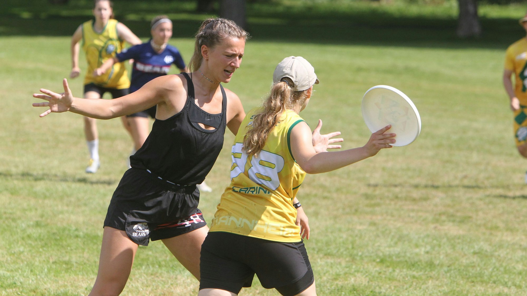 Eine Spielszene: Eine Spielerin versucht mit ausgestreckten Armen ihre Gegnerin daran zu hindern, die Frisbee-Scheibe gut zu werfen.