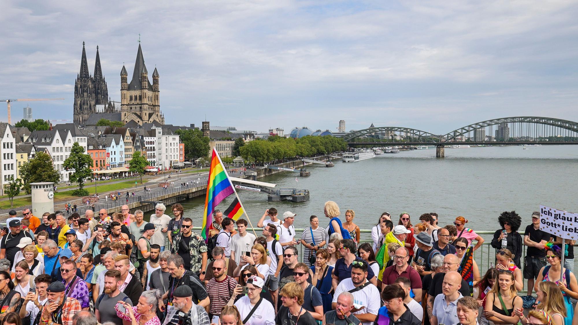 Eine Regenbogenflagge bei den Zuschauern beim CSD in Köln, iim Hintergrund der Kölner Dom