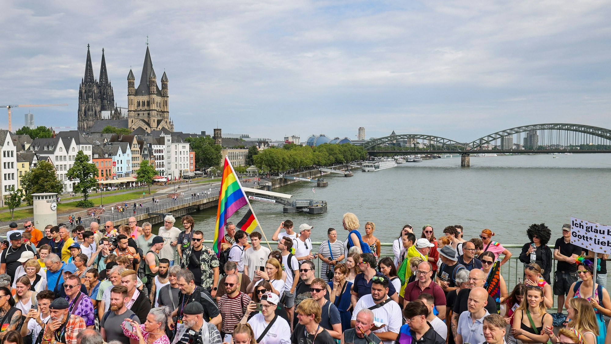 Eine Regenbogenflagge bei den Zuschauern beim CSD in Köln, iim Hintergrund der Kölner Dom