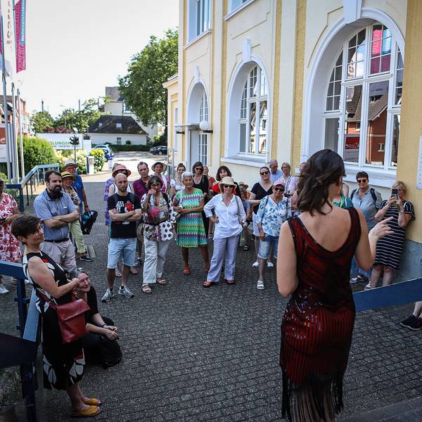 Eine junge Frau steht vor einer Menschengruppe am Erholungshaus