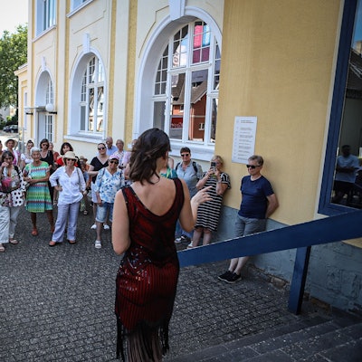 Eine junge Frau steht vor einer Menschengruppe am Erholungshaus