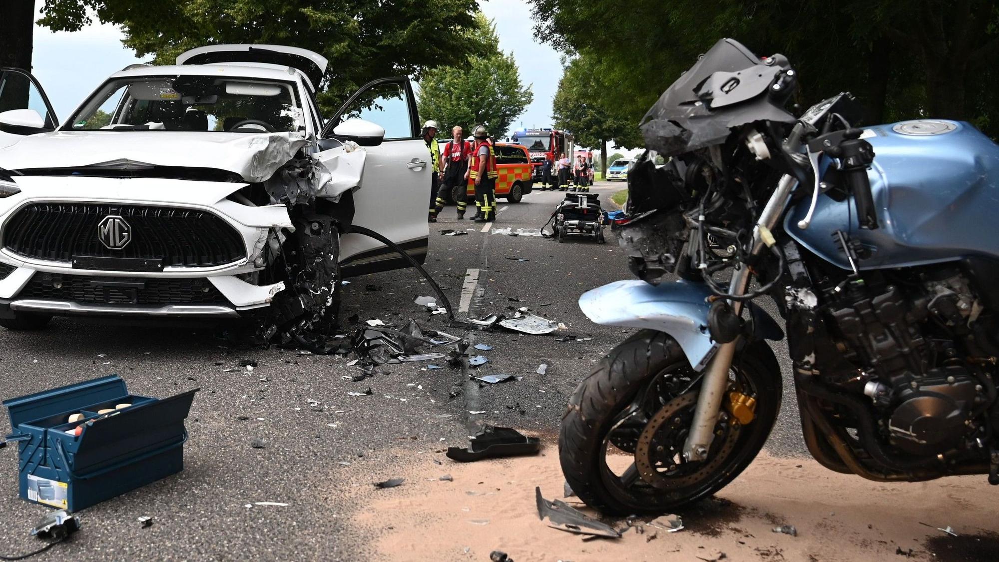 Das Bild zeigt die Unfallstelle in Elsdorf. Ein Motorrad und ein Auto stehen auf der Straße, mehrere Einsatzkräfte stehen an der Unfallstelle.
