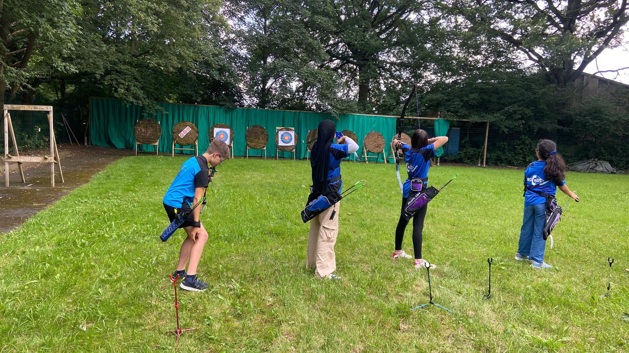 Kinder stehen in einer Reihe und schießt mit Pfeil und Bogen.