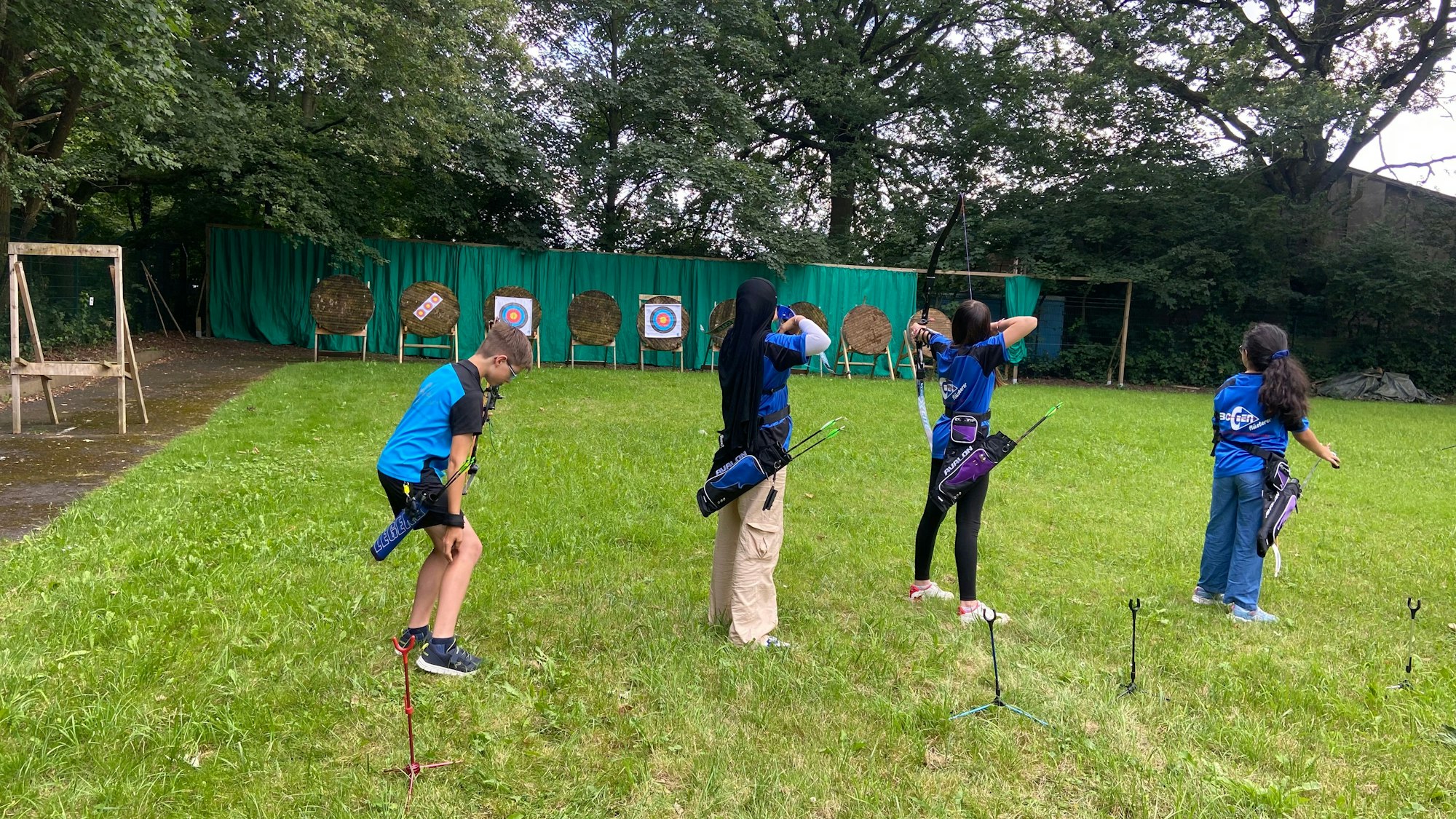 Kinder stehen in einer Reihe und schießt mit Pfeil und Bogen.