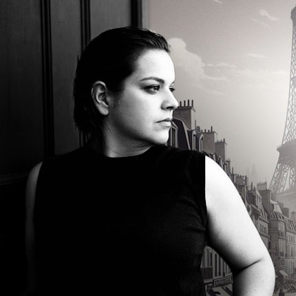 Auf dem Bild ist Rosa Halina Dahm zu sehen, sie schaut verträumt zur Seite. Im Hintergrund ein historisches Bild der Stadt Paris und der Eifelturm im Hintergrund. Das Bild ist schwarz-weiß.