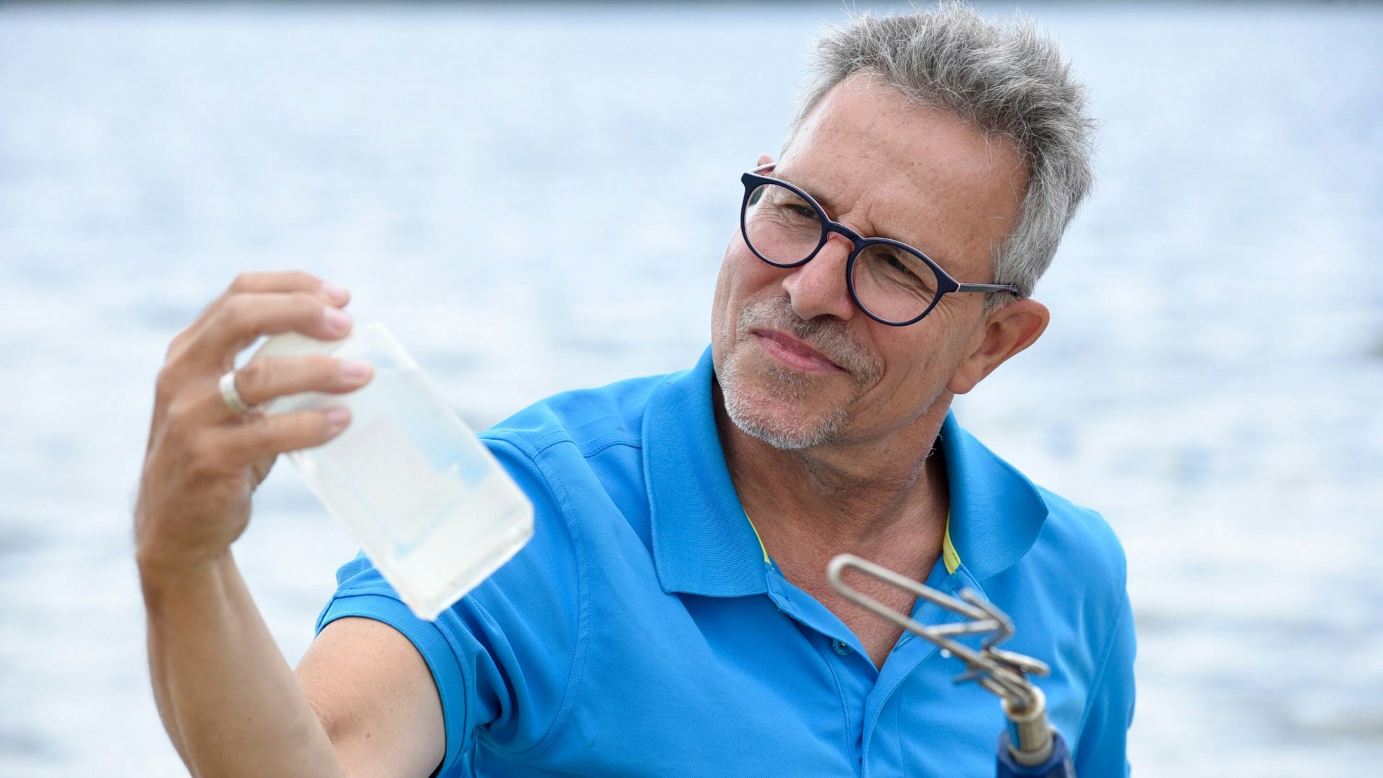 Ein Mann an einem See hält eine Flasche in der Hand.
