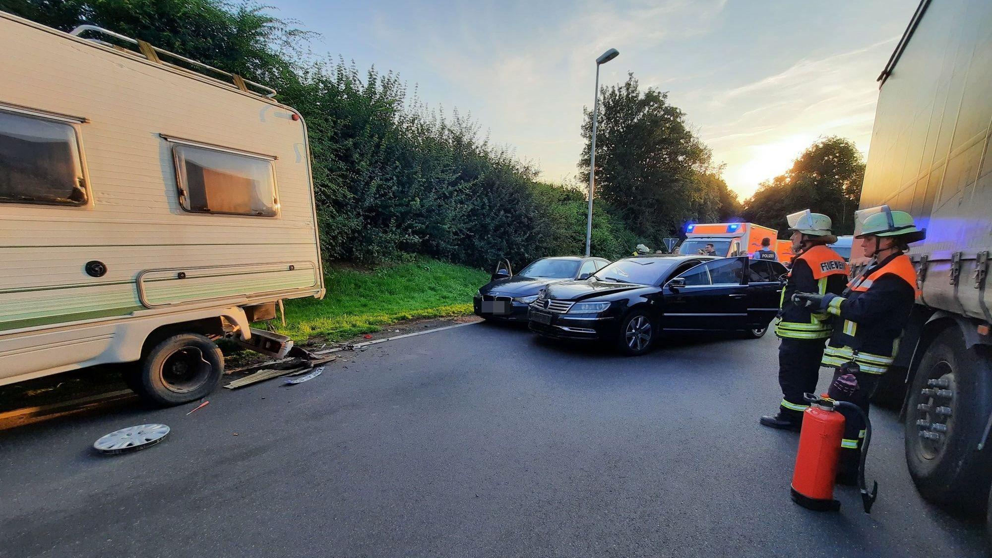 Drei Feuerwehrleute stehen in der Nähe von drei verbeulten Autos.