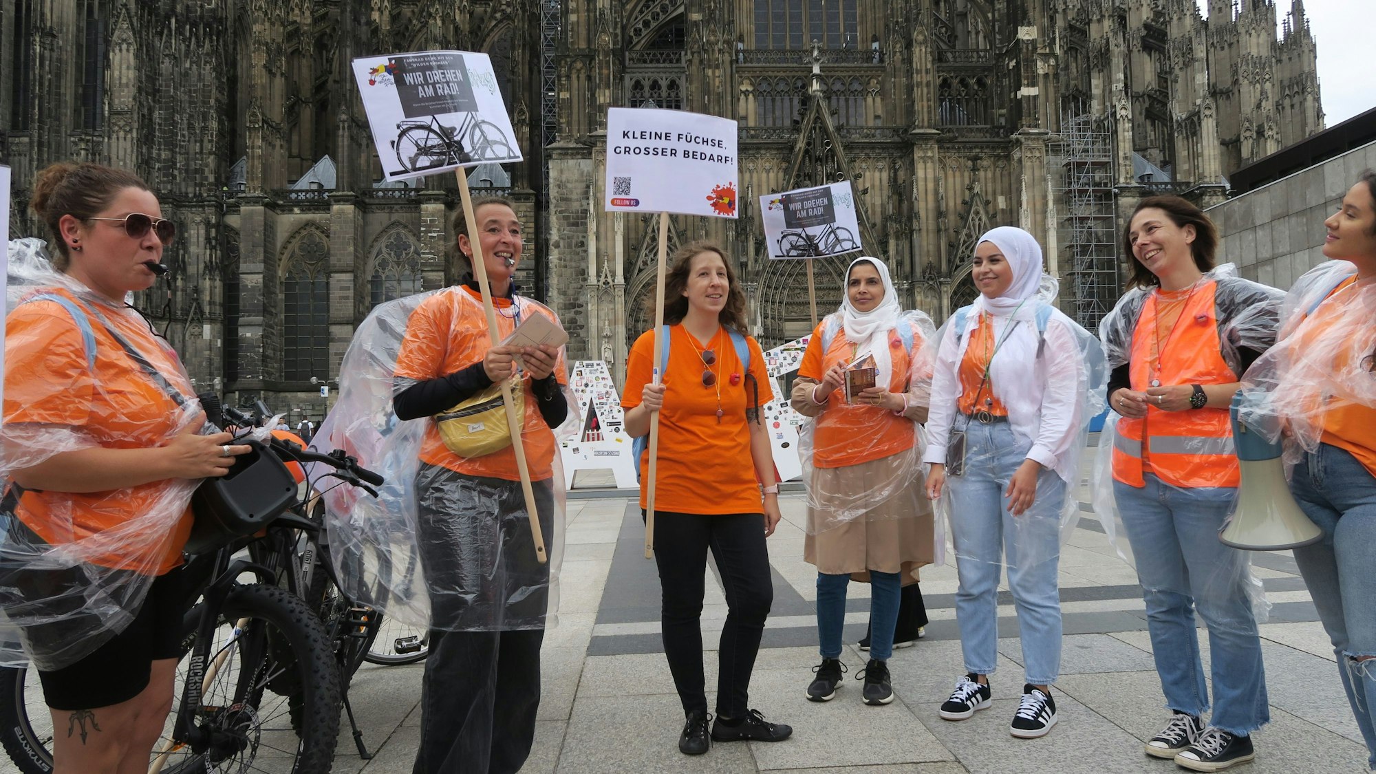 Sieben Frauen stehen auf der Domplatte, sie tragen orange T-Shirts und halten Demo-Plakate in die Höhe.
