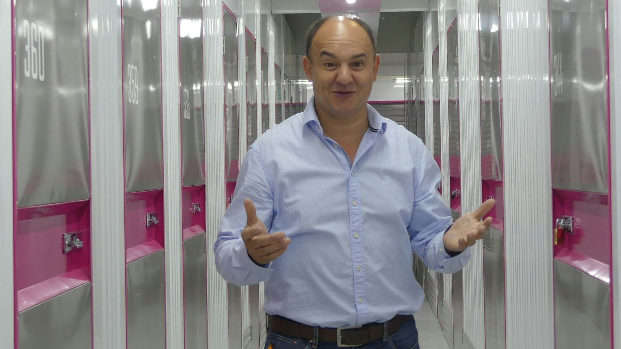 Ein Mann im hellblauen Hemd und schütterem Haar steht mit erhobenen Händen in einem schmalen Gang zwischen mietbaren Lagerboxen.