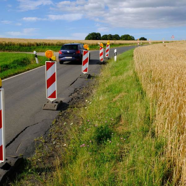 Am Rand der maroden Kreisstraße 58 zwischen Harzheim und Eiserfey stehen rot-weiße Warnbaken; ein Auto fährt vorbei.
