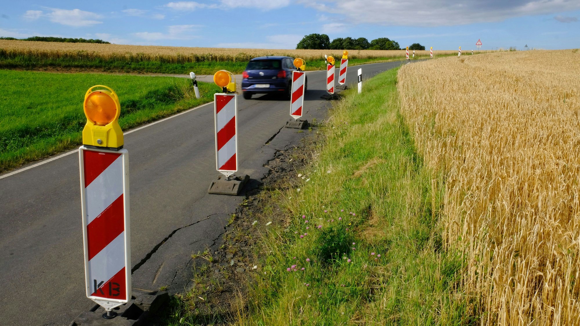 Am Rand der maroden Kreisstraße 58 zwischen Harzheim und Eiserfey stehen rot-weiße Warnbaken; ein Auto fährt vorbei.