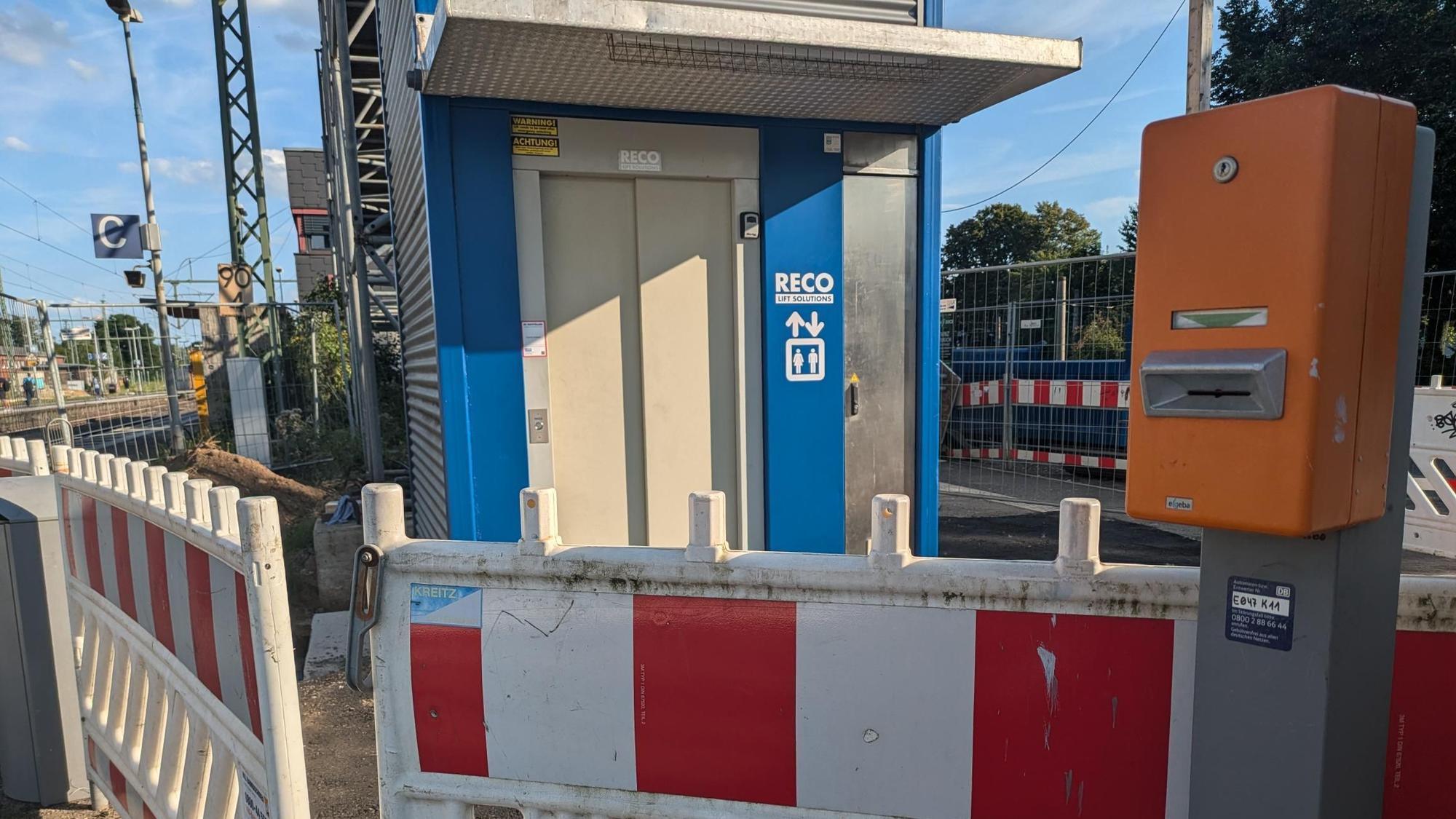 Ein Eingangsbereich eines Aufzugs auf einem Bahnsteig. Vor dem Aufzug stehen rot-weiße Absperrbaken.