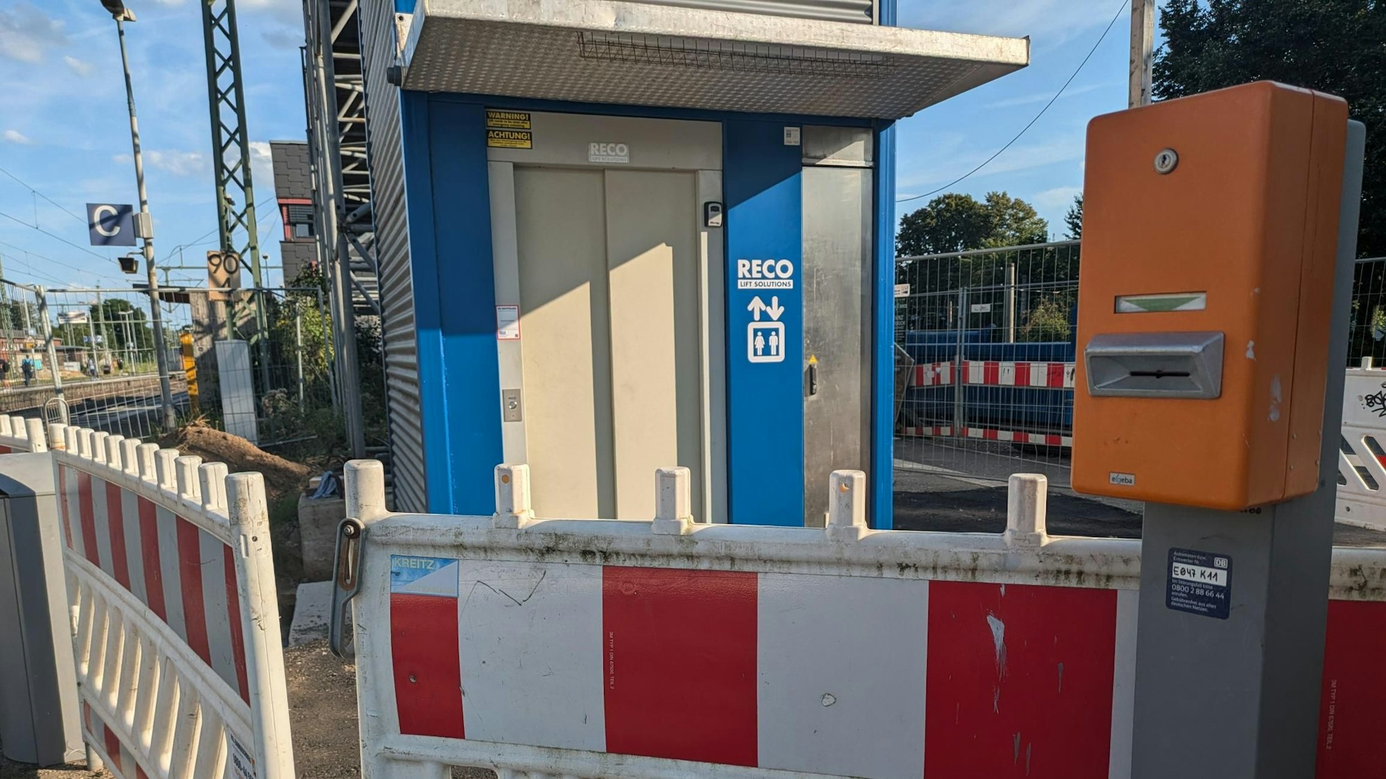 Ein Eingangsbereich eines Aufzugs auf einem Bahnsteig. Vor dem Aufzug stehen rot-weiße Absperrbaken.