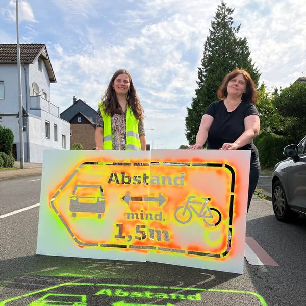 Zwei Frauen stehen hinter einem Sprühsymbol auf der Straße.