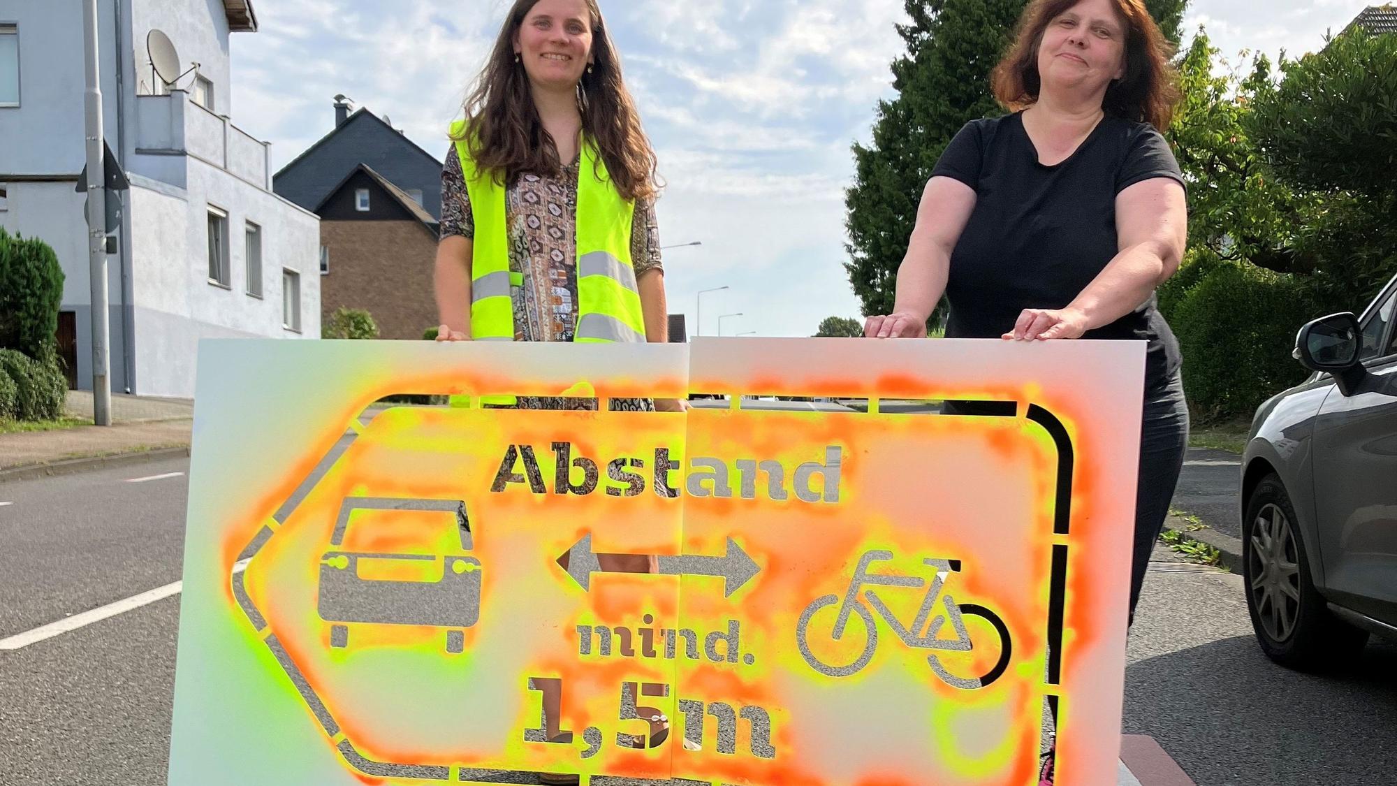 Zwei Frauen stehen hinter einem Sprühsymbol auf der Straße.